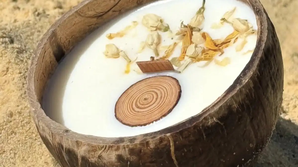 Bougie parfumée Luminante en noix de coco décorée de fleurs séchées, posée sur le sable