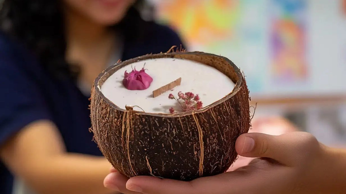 Femme tenant une bougie parfumée Luminante en noix de coco devant des dessins d’enfants