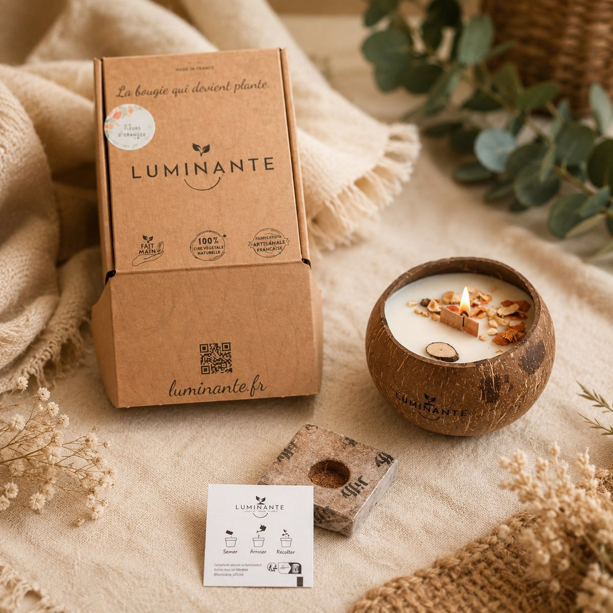 Bougie Luminante allumée avec sa boîte kraft, son bloc de terreau et sa carte de plantation Semer, Arroser, Récolter