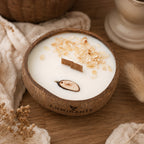 Bougie Luminante Fleur de Coton posée sur une table en bois avec un plaid et des fleurs séchées