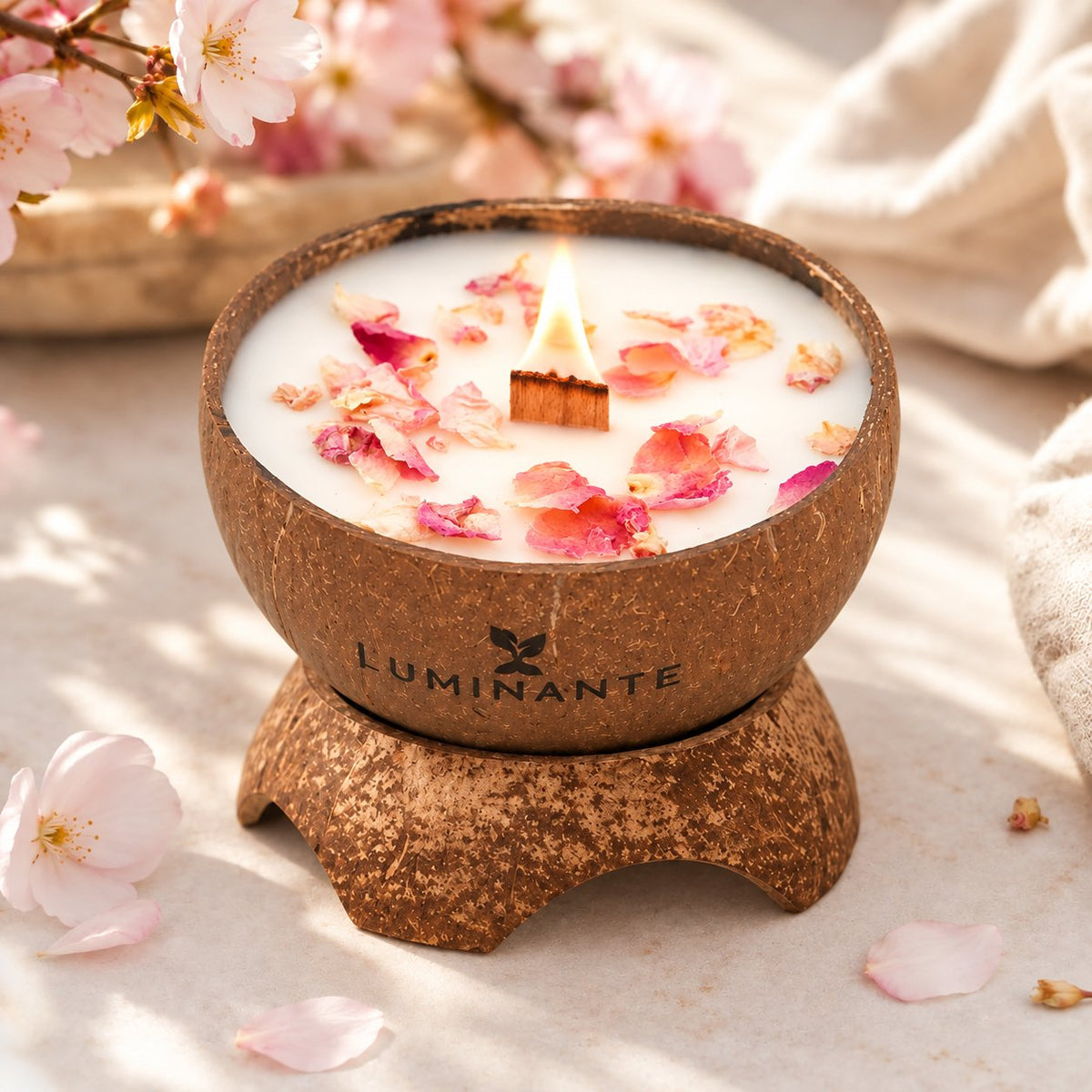 Bougie Luminante Fleur de Cerisier allumée entourée de pétales de fleurs de cerisier roses et jaunes