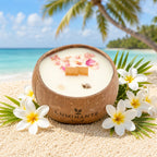 Bougie Luminante Fleur de Tiaré posée sur le sable, entourée de fleurs blanches et de palmes