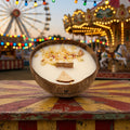 Bougie Luminante Pomme d'Amour posée devant une grande roue et un manège illuminés