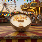 Bougie Luminante Pomme d'Amour posée devant une grande roue et un manège illuminés