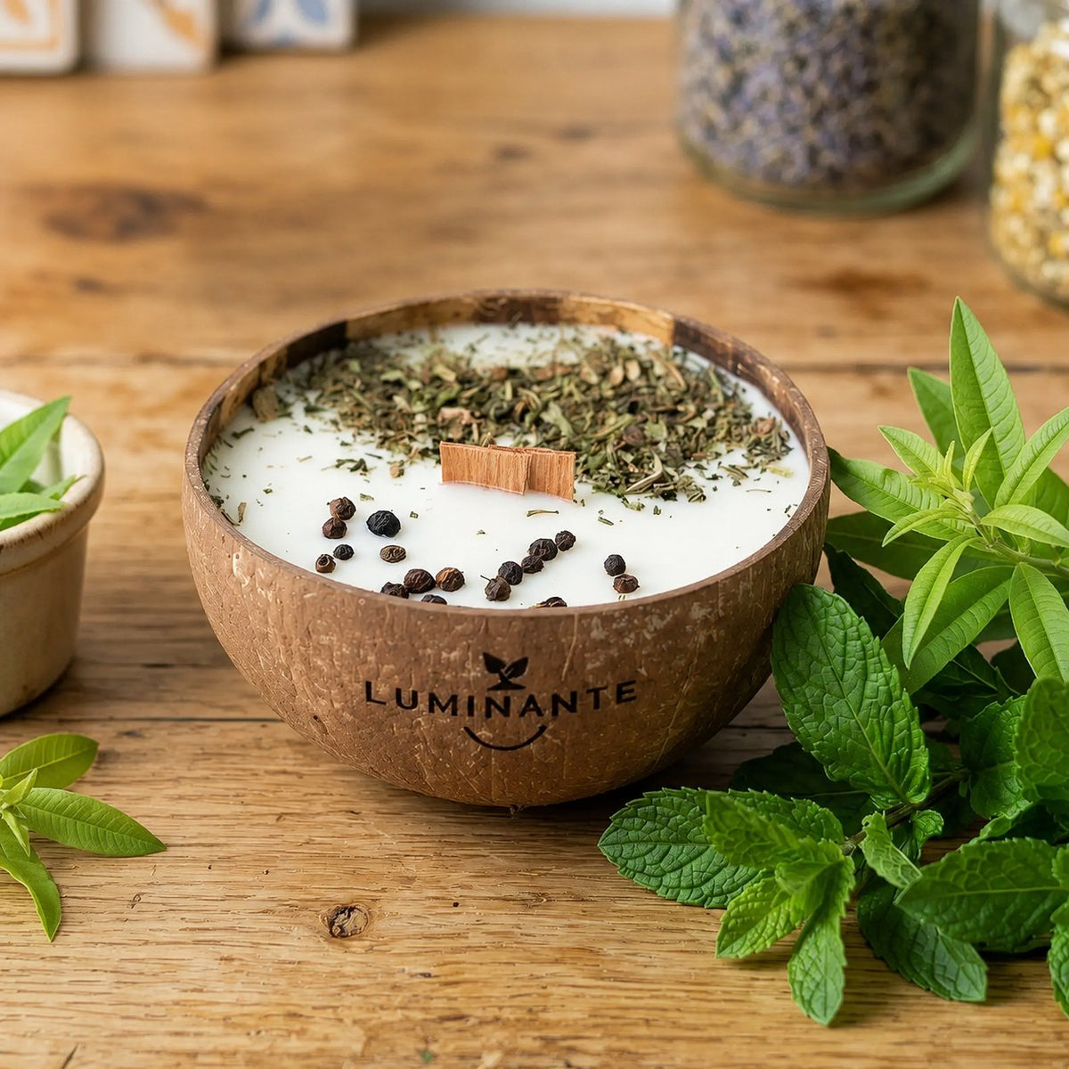 Bougie Luminante Verveine Menthe dans son contenant en noix de coco, feuilles séchées et grains de poivre sur la cire