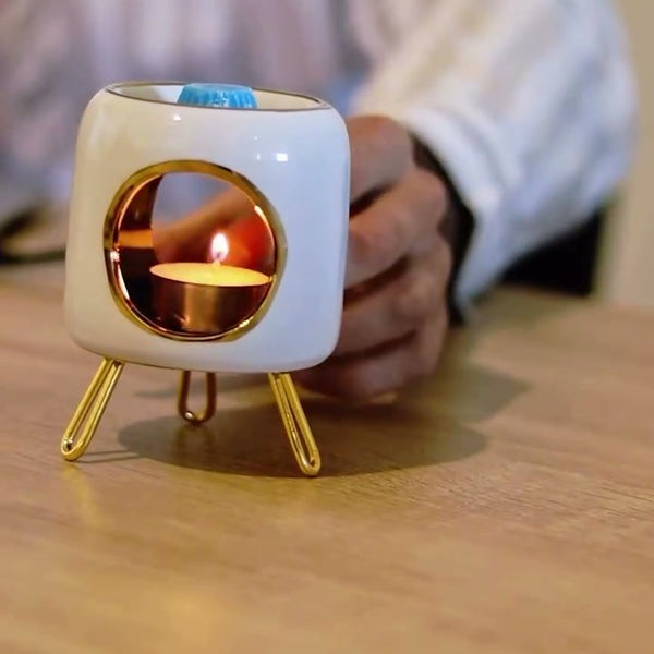 Brûle-parfum Luminante en céramique blanche allumé, posé sur un bureau