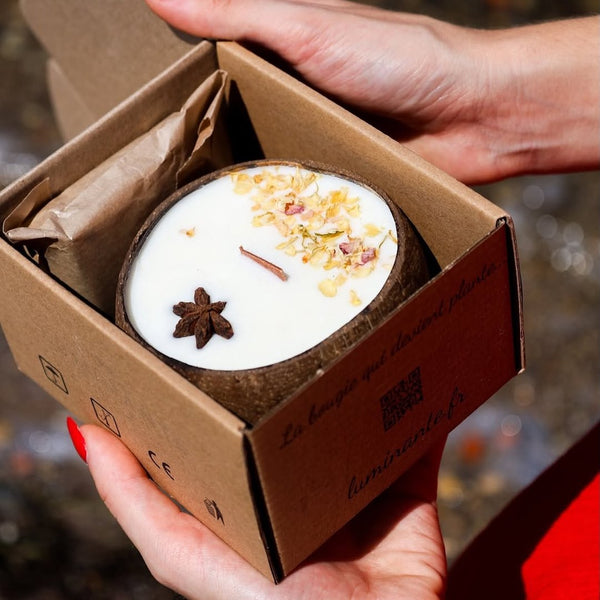 Mains ouvrant un coffret Luminante contenant une bougie décorée de fleurs séchées