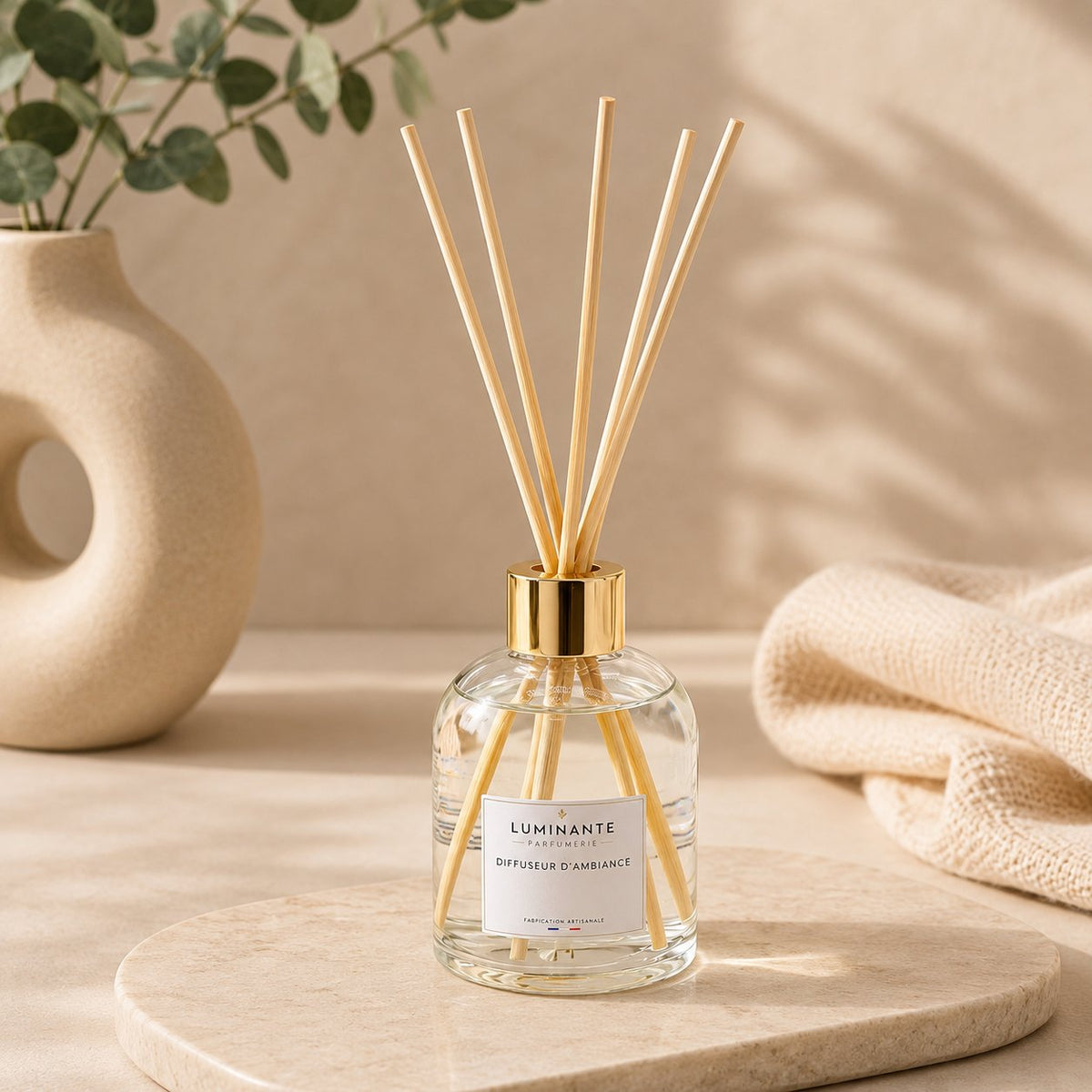 Diffuseur d'ambiance Luminante, flacon en verre à bouchon doré et bâtonnets en rotin