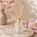 Diffuseur d'ambiance Luminante Fleur de cerisier, entouré de branches de cerisier en fleurs et de pétales roses