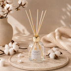Diffuseur d'ambiance Luminante Fleur de coton sur un plateau, entouré de branches de coton et d'un plaid écru
