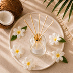 Diffuseur d'ambiance Luminante Tiaré-coco vu de dessus sur un plateau, fleurs blanches et noix de coco
