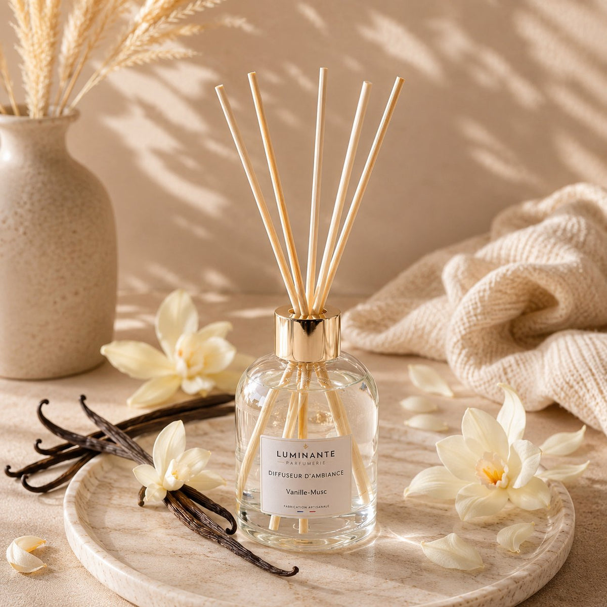 Diffuseur d'ambiance Luminante Vanille-Musc de face sur un plateau, gousses de vanille et fleurs crème