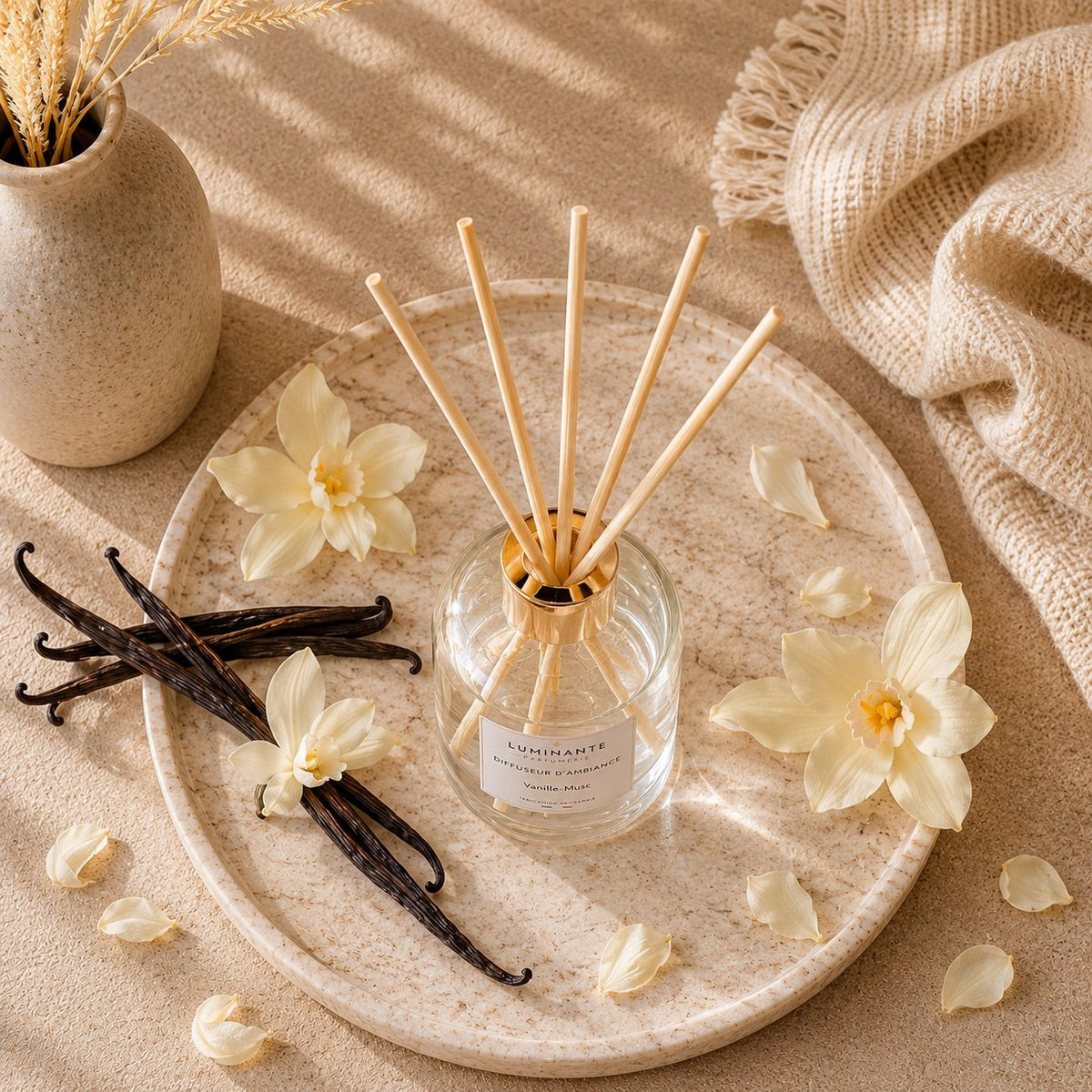 Diffuseur d'ambiance Luminante Vanille-Musc sur un plateau, entouré de gousses de vanille et de fleurs crème