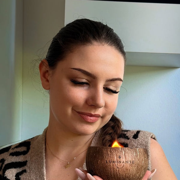 Femme souriante tenant une bougie Luminante allumée dans sa coque de noix de coco