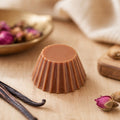 Fondant parfumé Luminante Bois de Oud, pastille de cire cannelée posée sur un plan en bois clair, entre des gousses de vanille et des boutons de rose séchés