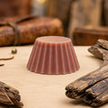 Fondant parfumé Luminante Cuir et bois, pastille de cire cannelée posée sur un plan en bois clair, entre des morceaux de bois et un étui en cuir