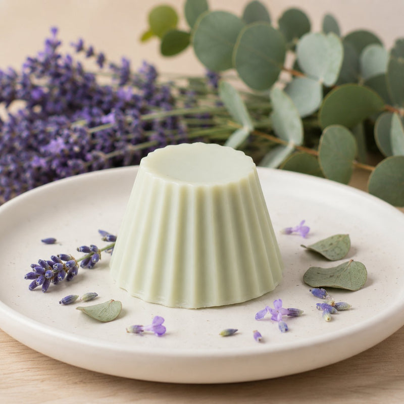 Fondant parfumé Luminante Eucalyptus Lavande, pastille de cire vert pâle sur une assiette en céramique, entourée de brins de lavande et de feuilles d'eucalyptus