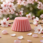 Fondant parfumé Luminante Fleur de Cerisier posé sur une table en bois devant un cerisier en fleurs