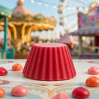 Fondant parfumé Luminante Pomme d'Amour posé sur un guichet de fête foraine, devant un manège et une grande roue