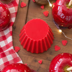Fondant parfumé Luminante Pomme d'Amour, pastille de cire rouge vue de dessus sur une table en bois, entourée de pommes d'amour et de petits cœurs