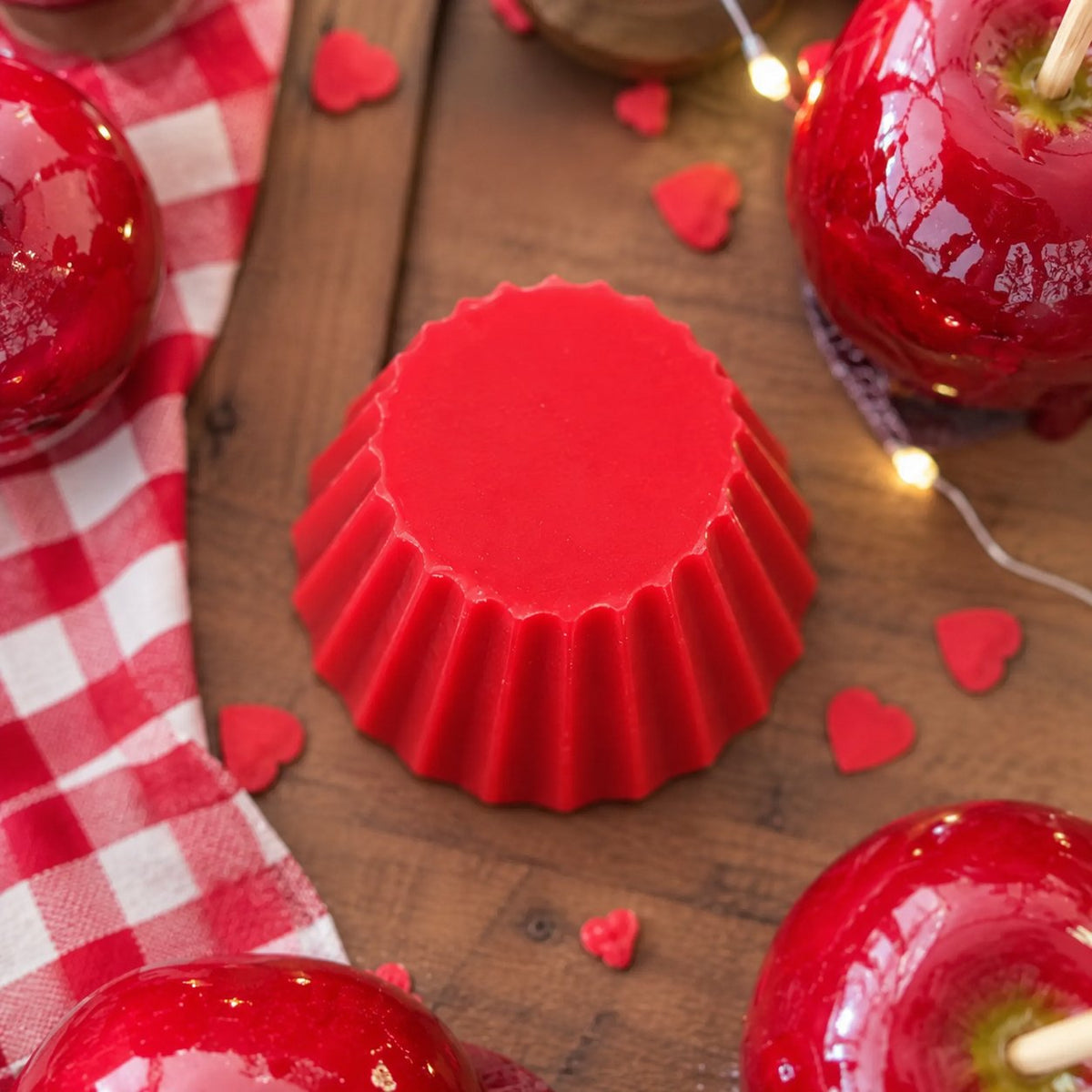 Fondant parfumé Luminante Pomme d'Amour, pastille de cire rouge vue de dessus sur une table en bois, entourée de pommes d'amour et de petits cœurs