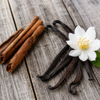Gousses de vanille, bâtons de cannelle et fleur blanche posés sur des planches de bois grisonnant