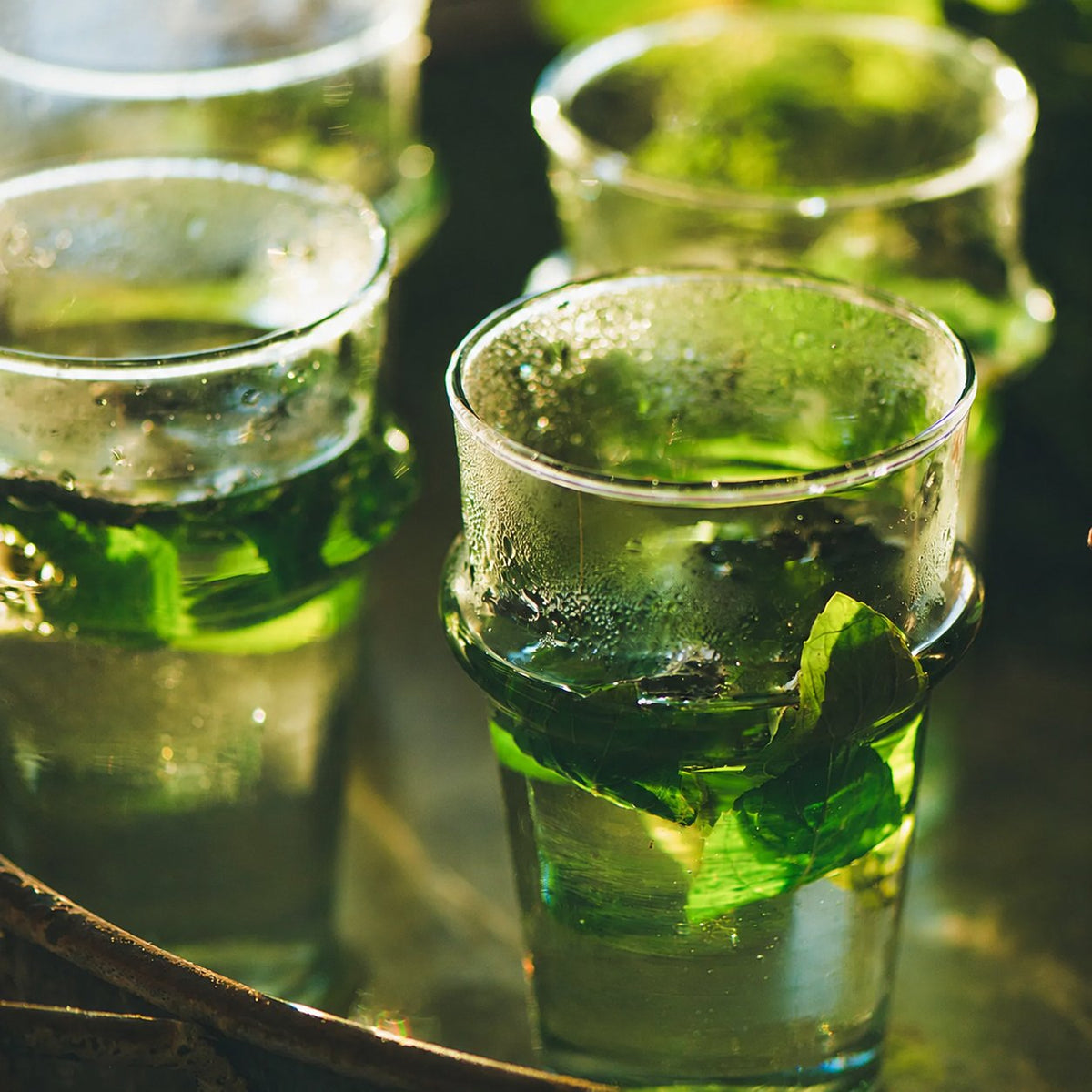Verres de thé à la menthe fraîche posés sur un plateau, à contre-jour