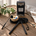 Kit d'accessoires Luminante posé sur une table en bois : éteignoir, briquet rechargeable, mouchette, ciseaux à mèche et plateau noir, avec sa boîte et une bougie en noix de coco