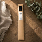 Étui kraft de bâtonnets noirs pour diffuseur Luminante, posé à plat sur une table en bois à côté d'une branche d'eucalyptus