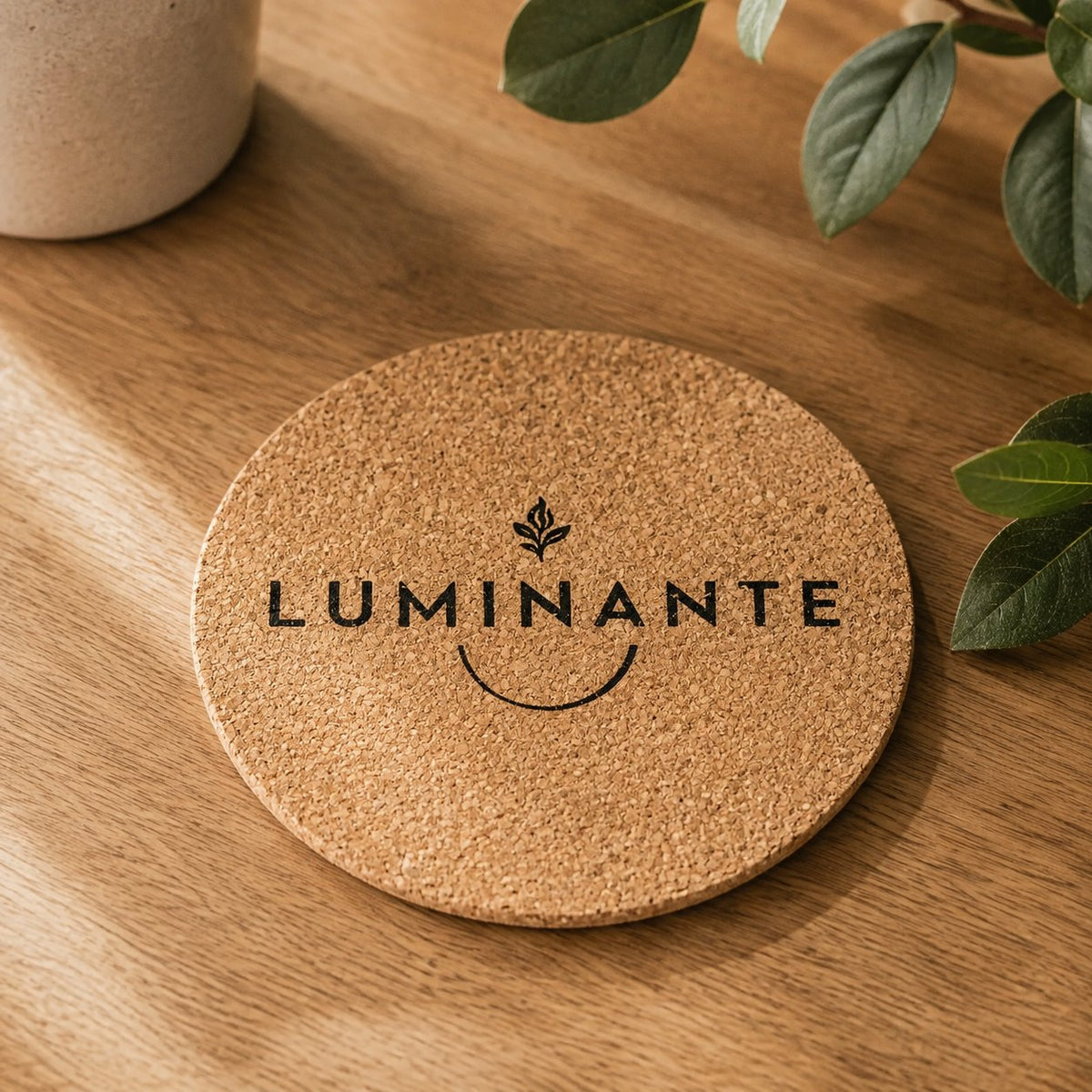 Dessous en liège rond Luminante gravé du logo de la marque, posé sur une table en bois clair