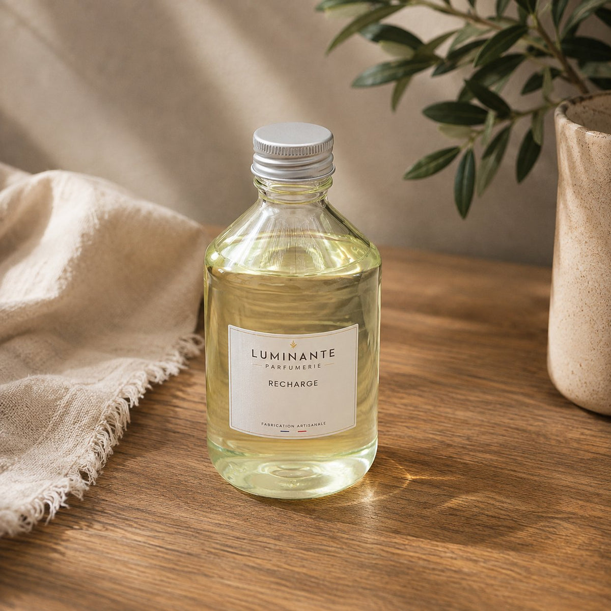 Recharge Luminante Bois de Oud, flacon en verre à bouchon argenté posé sur une table en bois