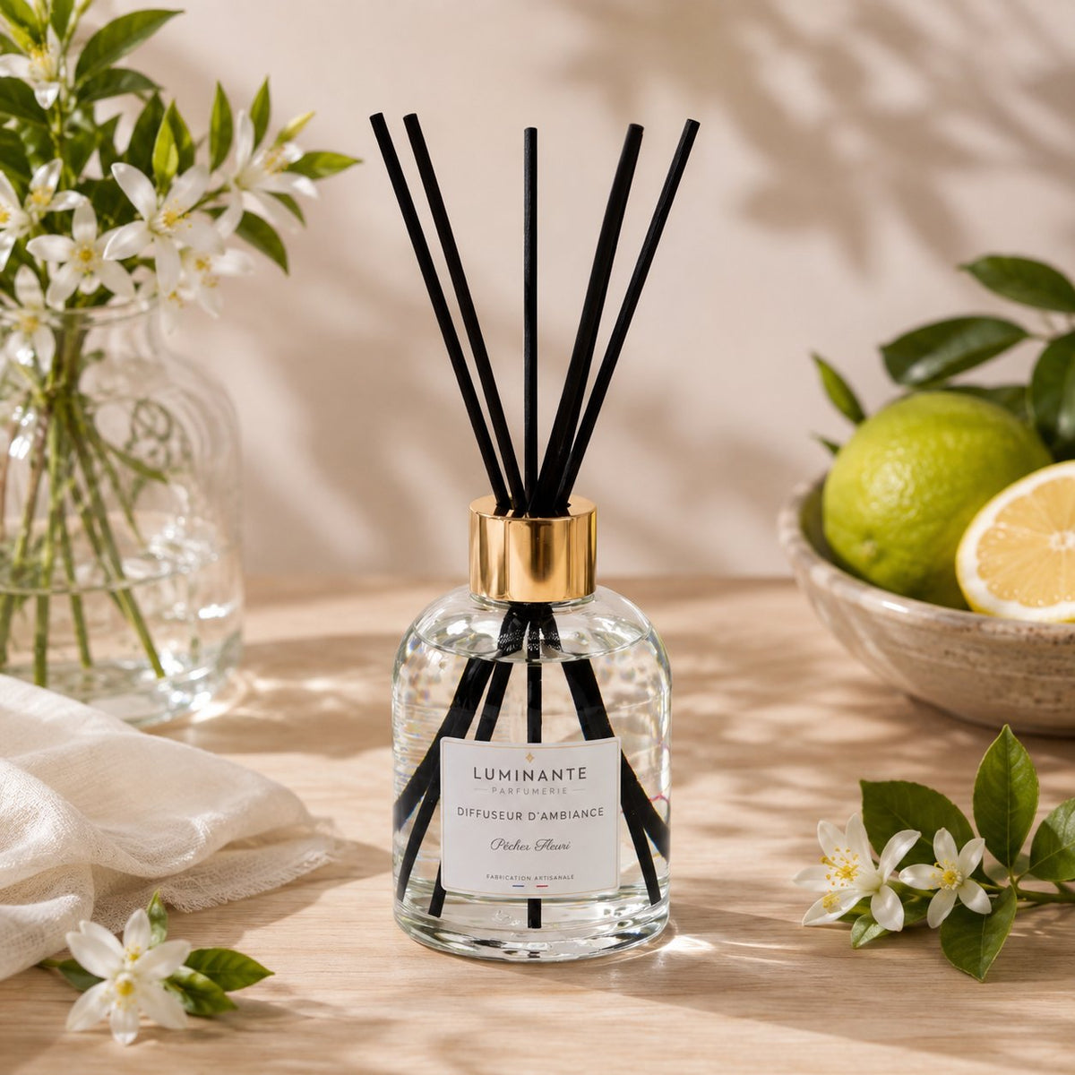 Diffuseur d'ambiance Luminante et ses bâtonnets, entouré de fleurs d'oranger et d'agrumes
