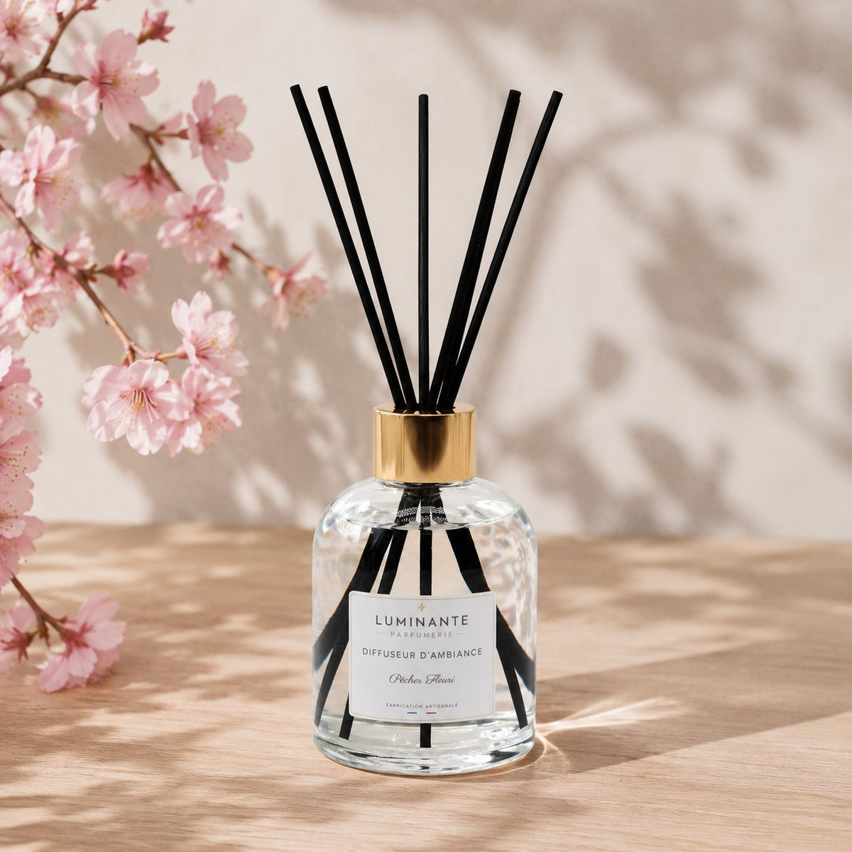 Diffuseur d'ambiance Luminante et ses bâtonnets, devant des branches de cerisier en fleurs
