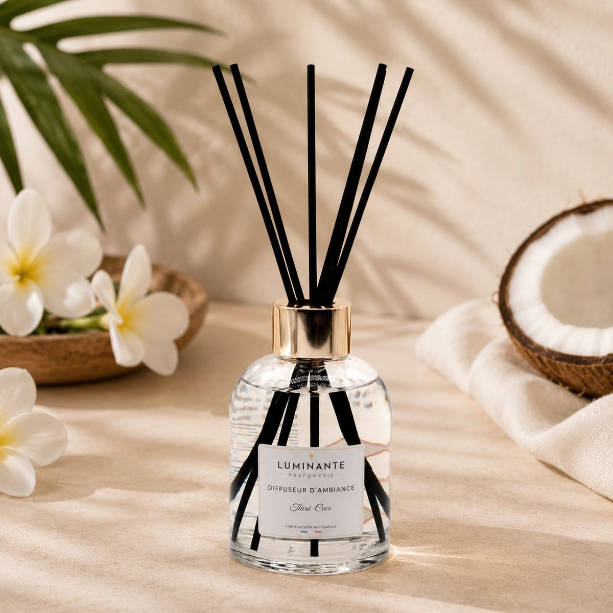 Diffuseur d'ambiance Luminante Tiaré-Coco et ses bâtonnets, entre des fleurs de tiaré et une noix de coco