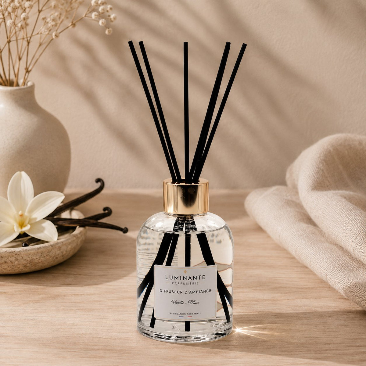 Diffuseur d'ambiance Luminante Vanille-Musc et ses bâtonnets, près de gousses de vanille