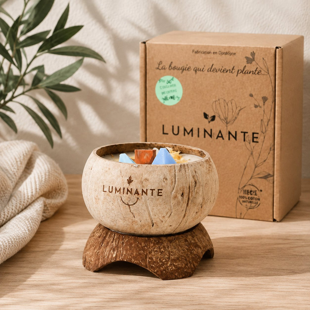 Bougie Luminante en noix de coco posée sur son socle, avec sa boîte kraft