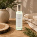 Vaporisateur d'ambiance Luminante Cèdre poudré, flacon à bouchon doré près d'une branche de cèdre