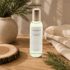 Vaporisateur d'ambiance Luminante Cèdre poudré, flacon à bouchon doré près d'une branche de cèdre