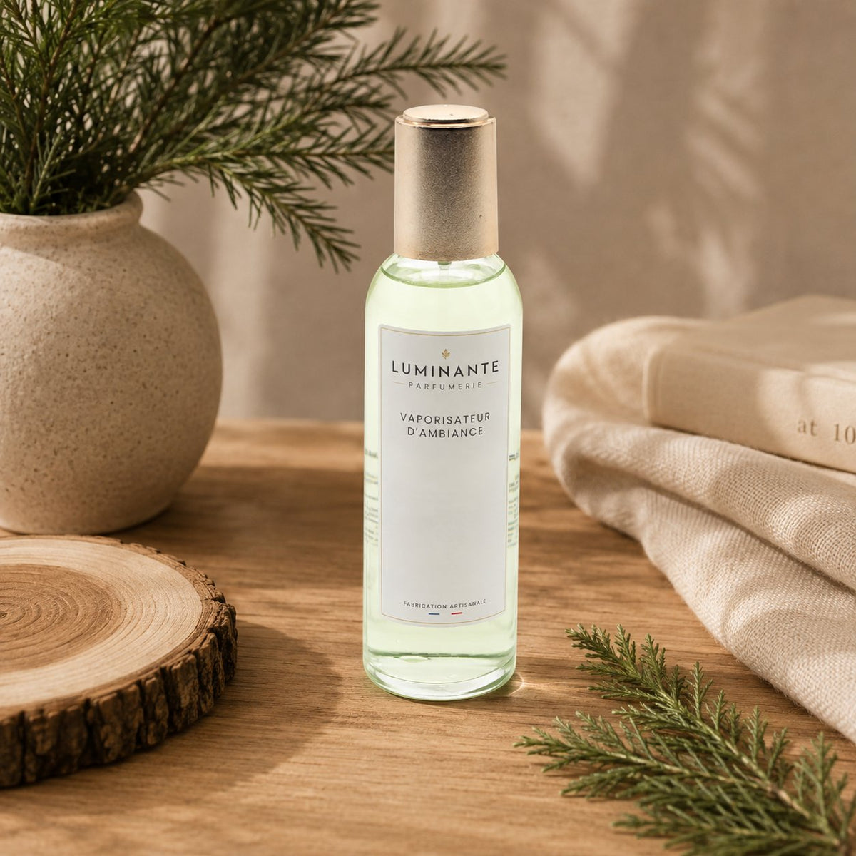 Vaporisateur d'ambiance Luminante Cèdre poudré, flacon à bouchon doré près d'une branche de cèdre