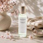 Vaporisateur d'ambiance Luminante Fleur de cerisier, flacon à bouchon doré sous des branches de cerisier en fleurs