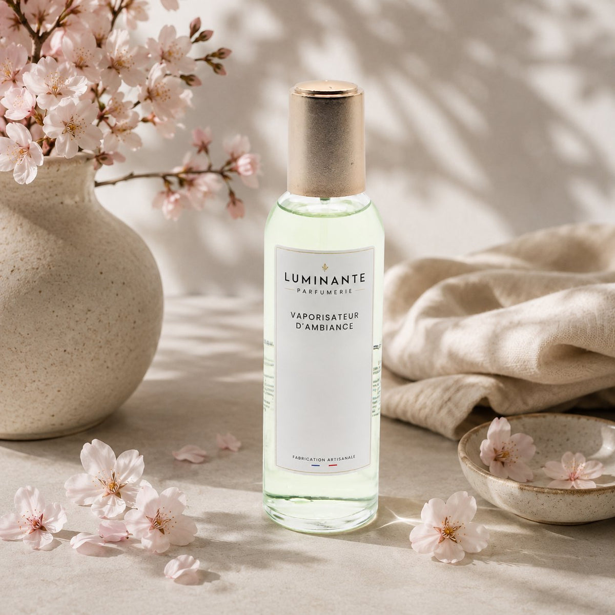 Vaporisateur d'ambiance Luminante Fleur de cerisier, flacon à bouchon doré sous des branches de cerisier en fleurs