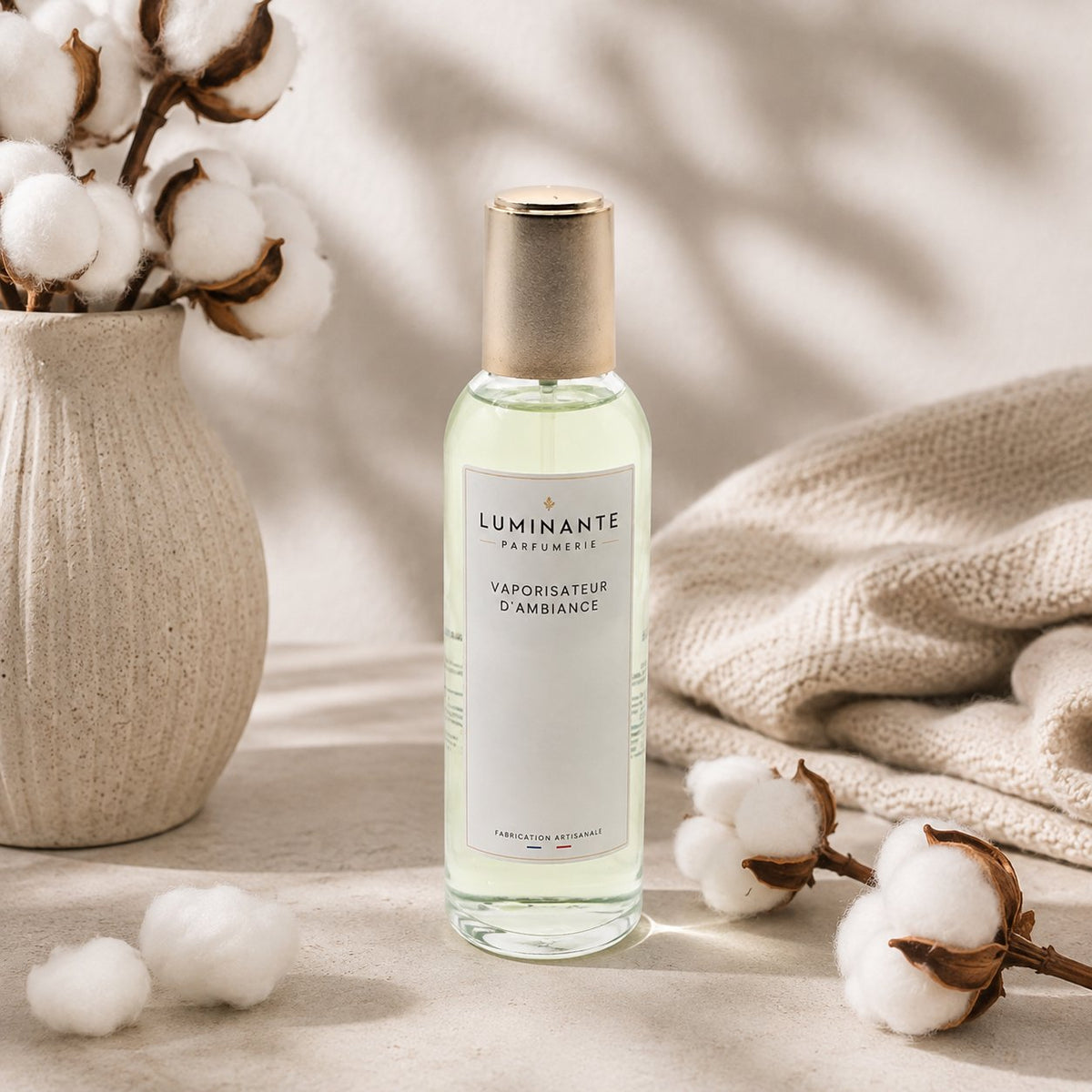 Vaporisateur d'ambiance Luminante Fleur de coton, flacon à bouchon doré près de fleurs de coton